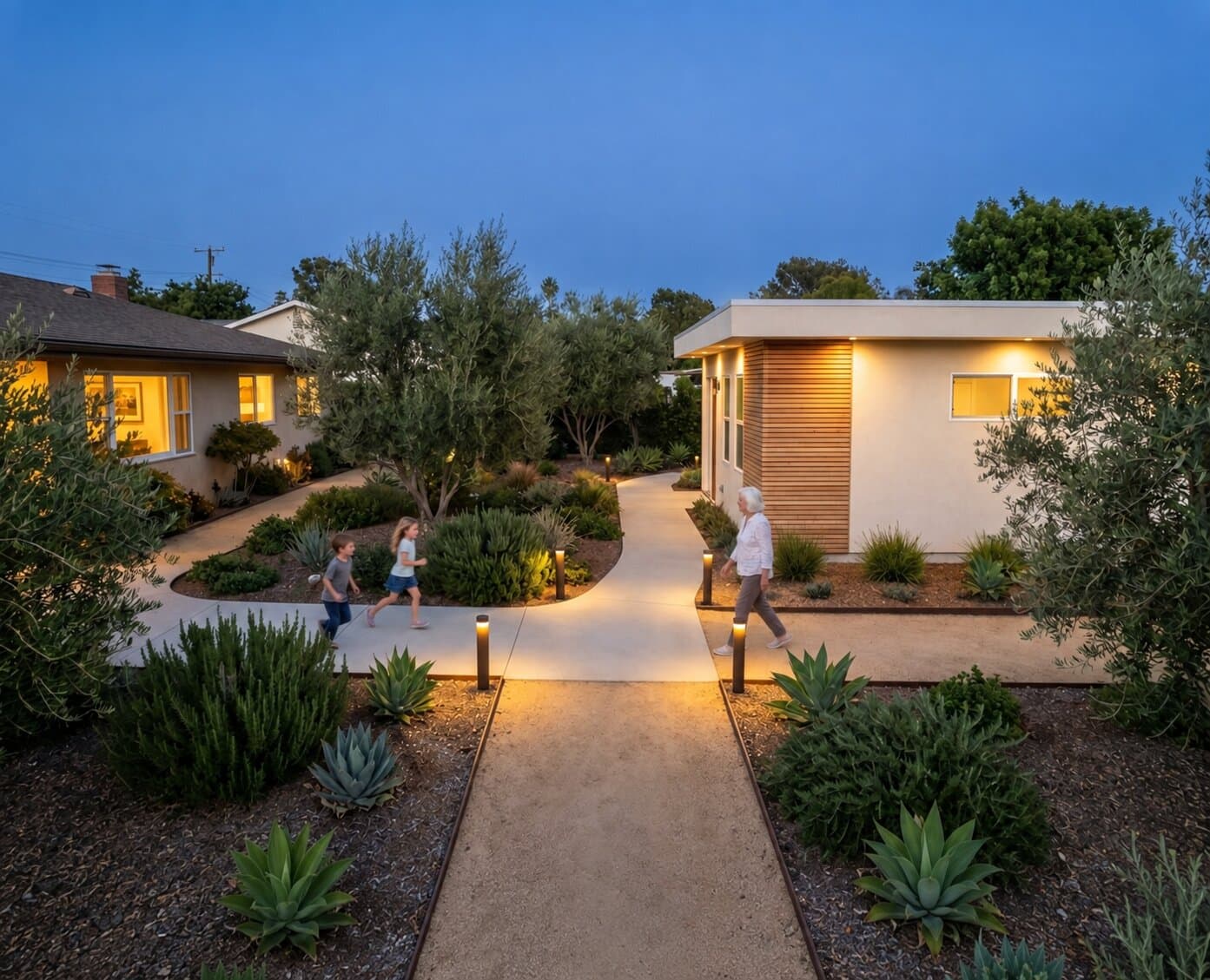 An elevated view of a Southern California backyard at dusk showing a single-story main house and a modern ADU connected by a lit walkway, with two children and their grandmother approaching each other on the path.
